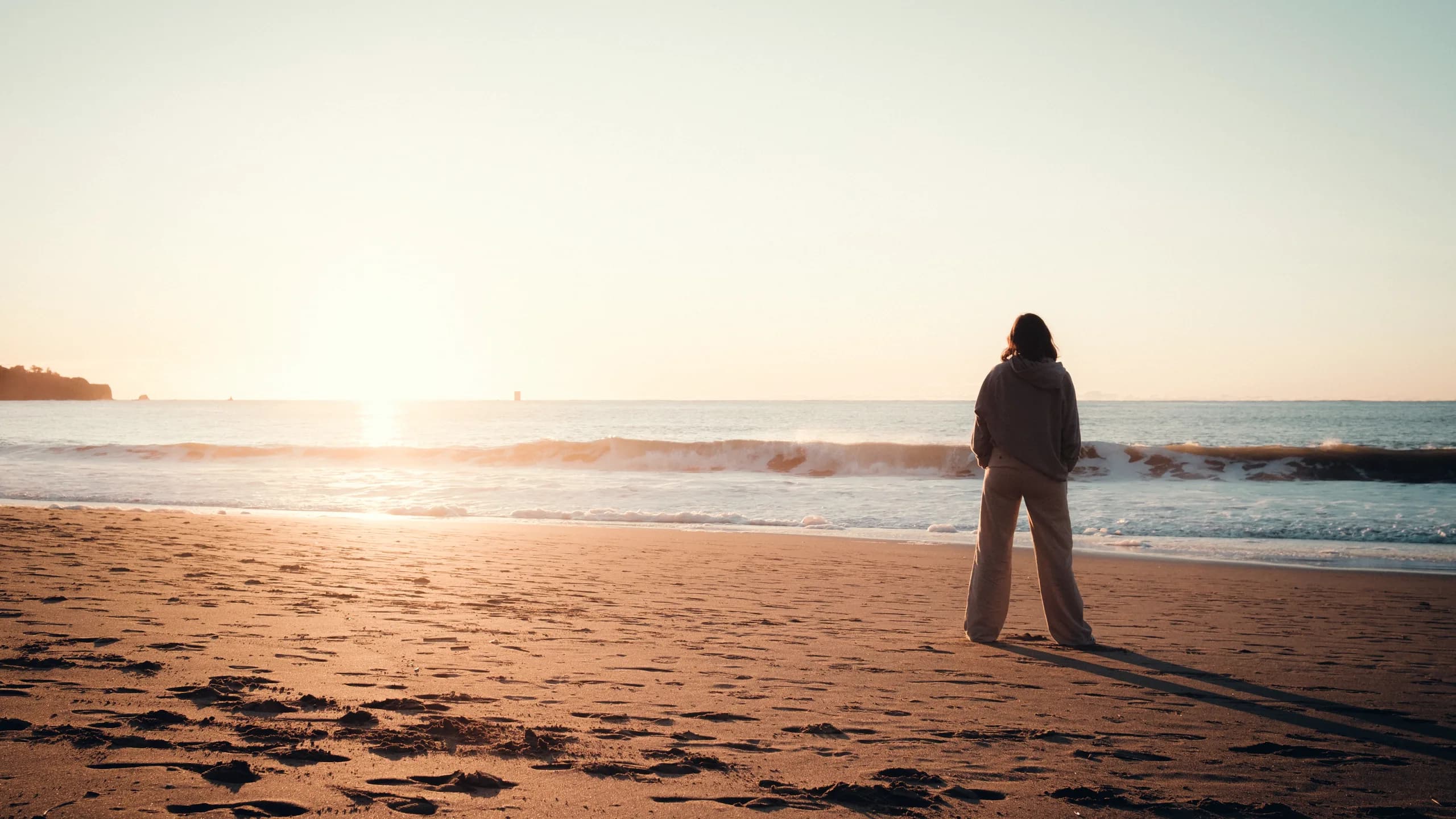 Person on a beach at golden hour, looking out at the calm ocean