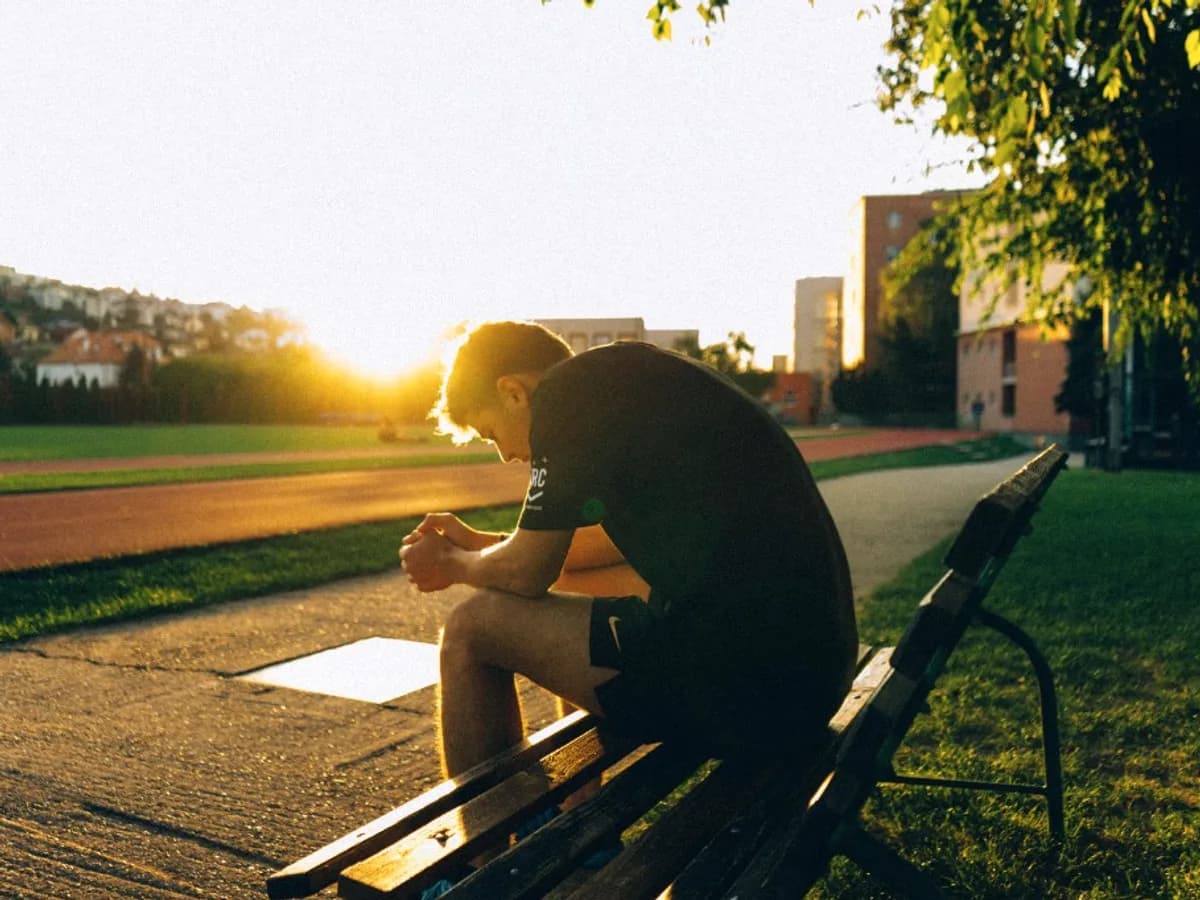 Young man sitting on a bench, looking down in thought