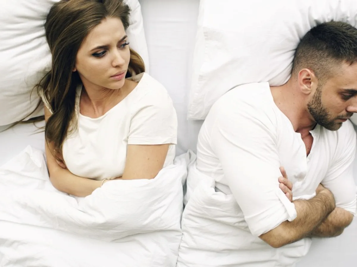 Couple lying in bed back to back, arms crossed